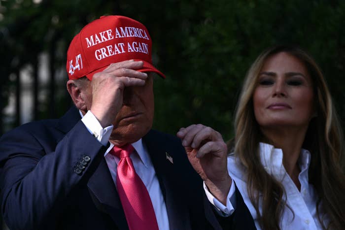 Two people in formal attire; one adjusts a 'Make America Great Again' cap