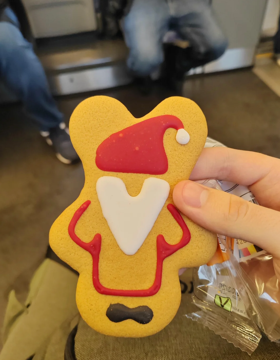 A person holds a gingerbread cookie, decorated with icing to look like a Santa outfit