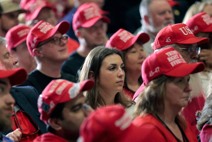 A crowd wearing red hats with political slogans listens attentively at a gathering