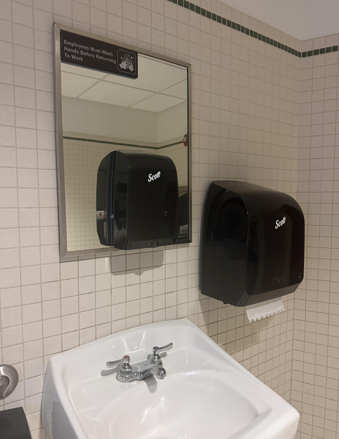 Bathroom sink with mirror above; soap dispenser is mounted on the mirror, blocking the majority of it