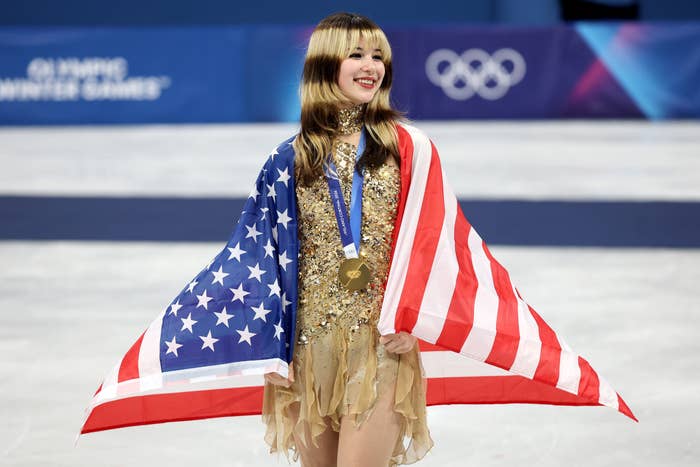 Figure skater connected  ice, wearing a sparkling dress, draped successful  a U.S. flag, Olympic rings successful  background