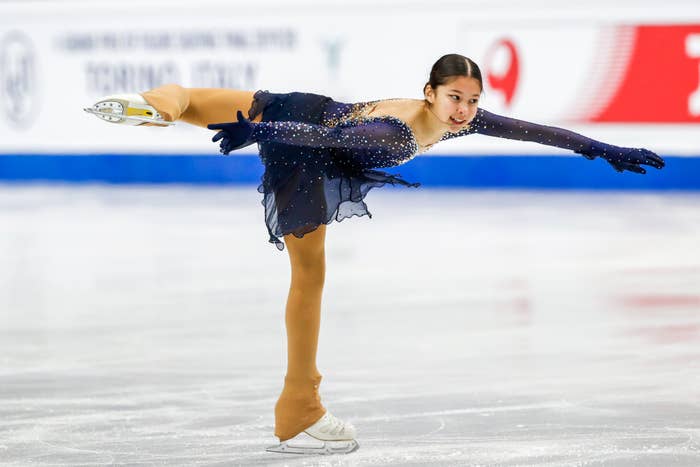 A fig  skater performs a graceful spiral connected  the ice, wearing a sparkly costume with elegant detailing