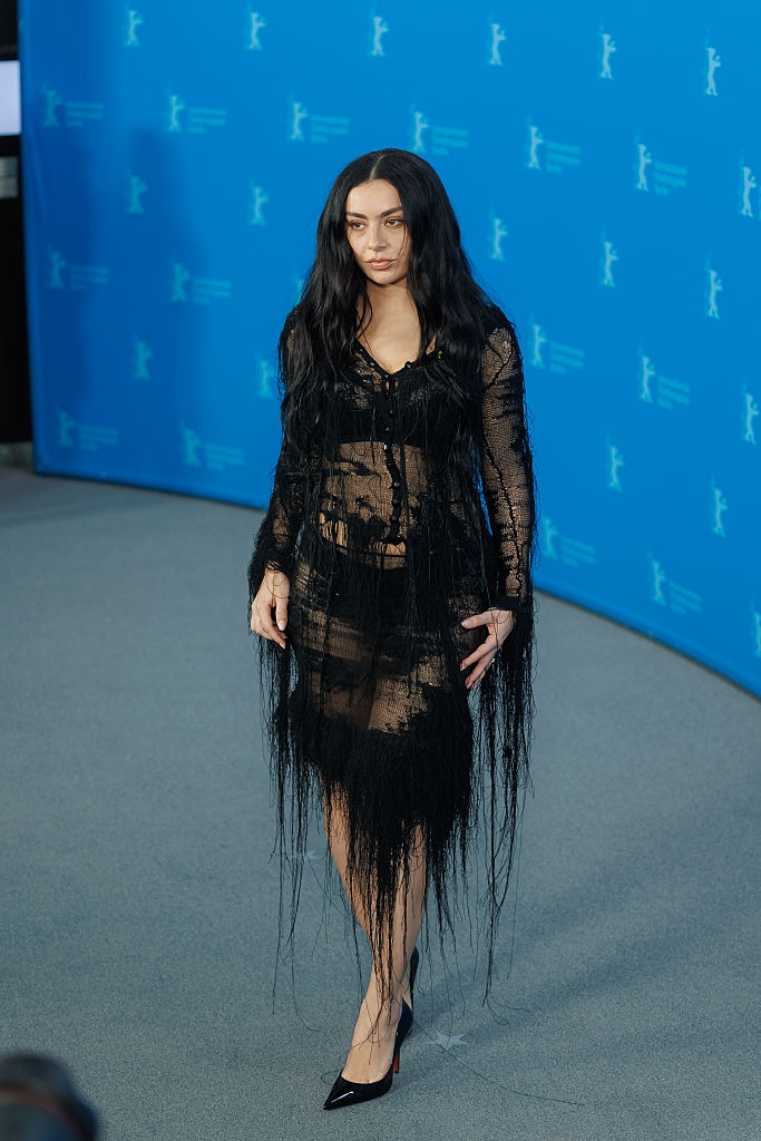 Person successful a sheer, black, long-sleeved formal with fringe details, connected a bluish carpet astatine a ceremonial event