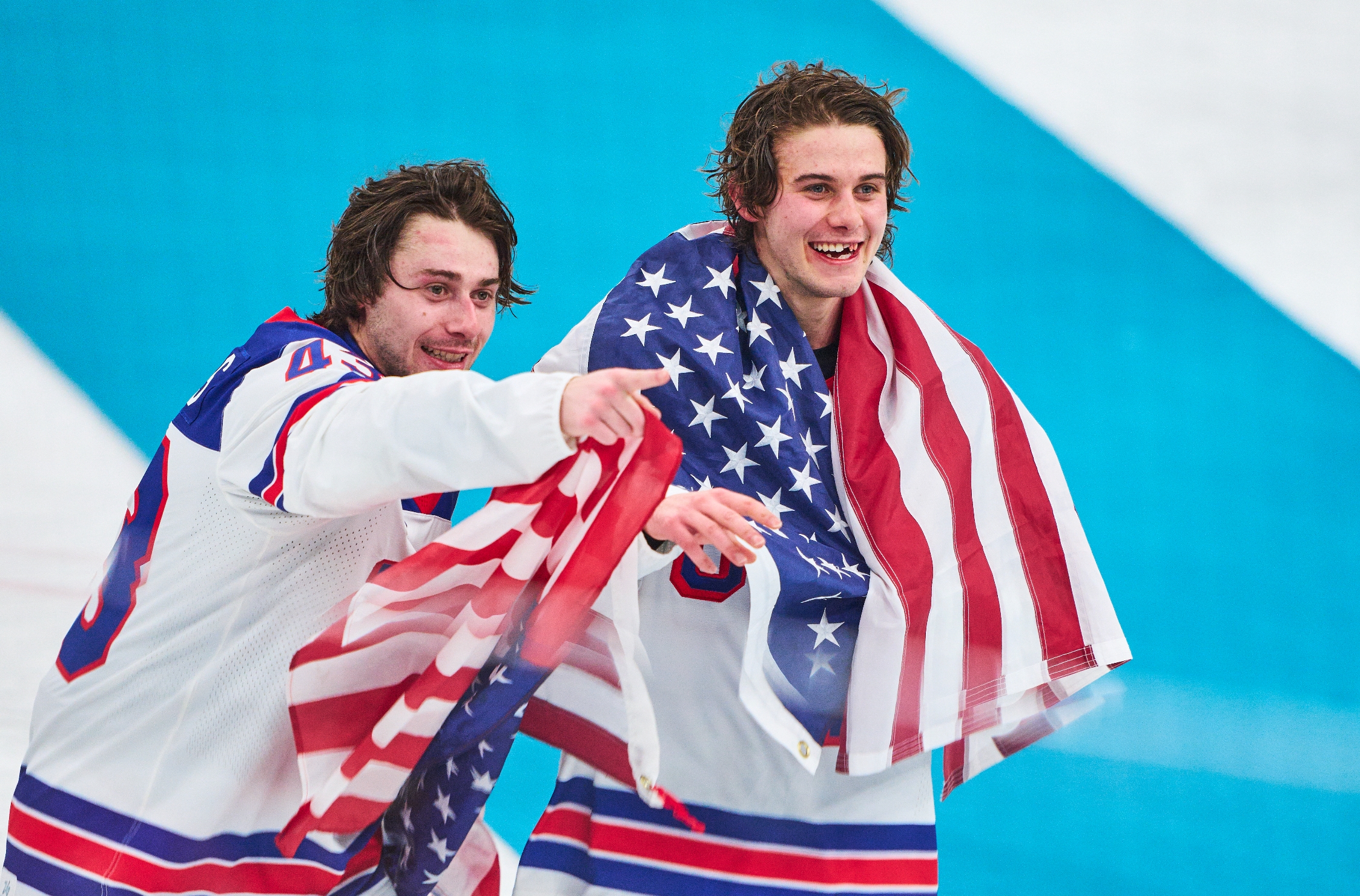 Two hockey players, wearing uniforms, joyfully observe  portion    1  draped successful  an American flag, pointing towards thing  off-camera