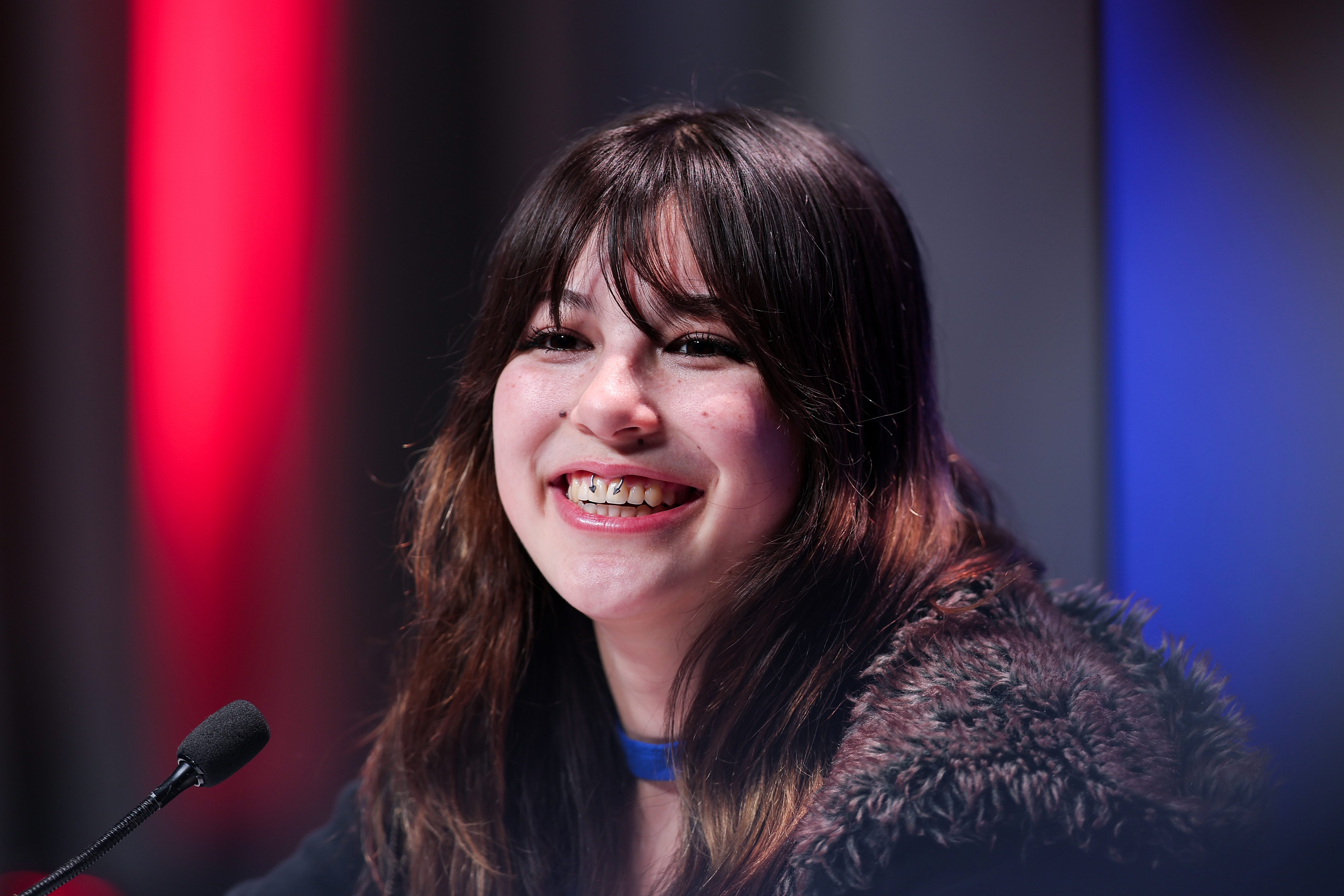 Person smiling astatine a podium, wearing a furry coat