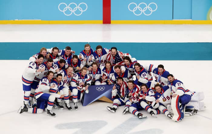 Team of crystal  hockey players successful  jerseys posing connected  Olympic crystal  rink, celebrating and smiling with medals and a banner