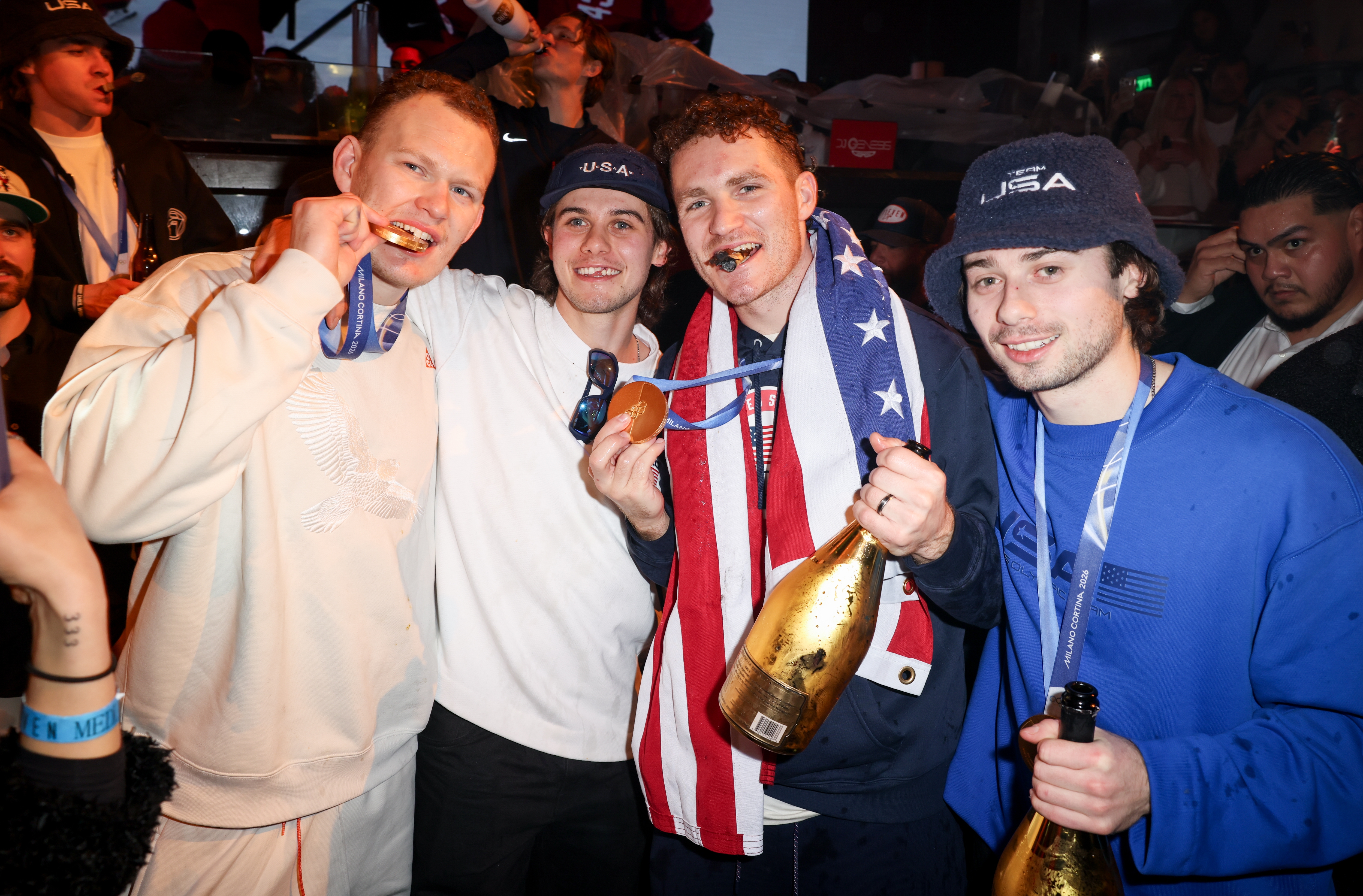 Four men observe  a sports victory, wearing casual covering  and USA-themed accessories, holding medals and champagne bottles