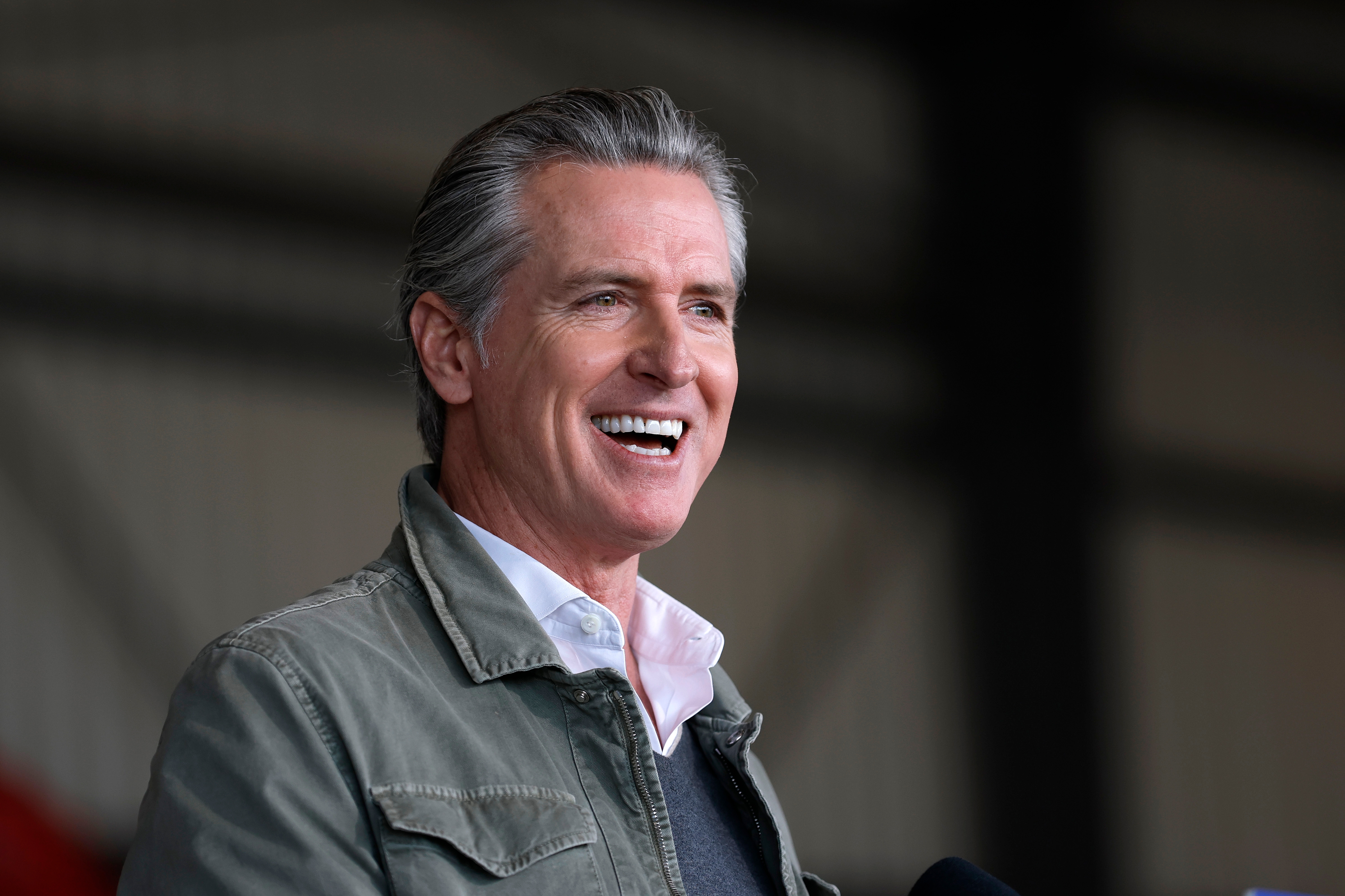 En person som snakker på et offentlig arrangement, iført en uformell jakke og skjorte, smiler varmt