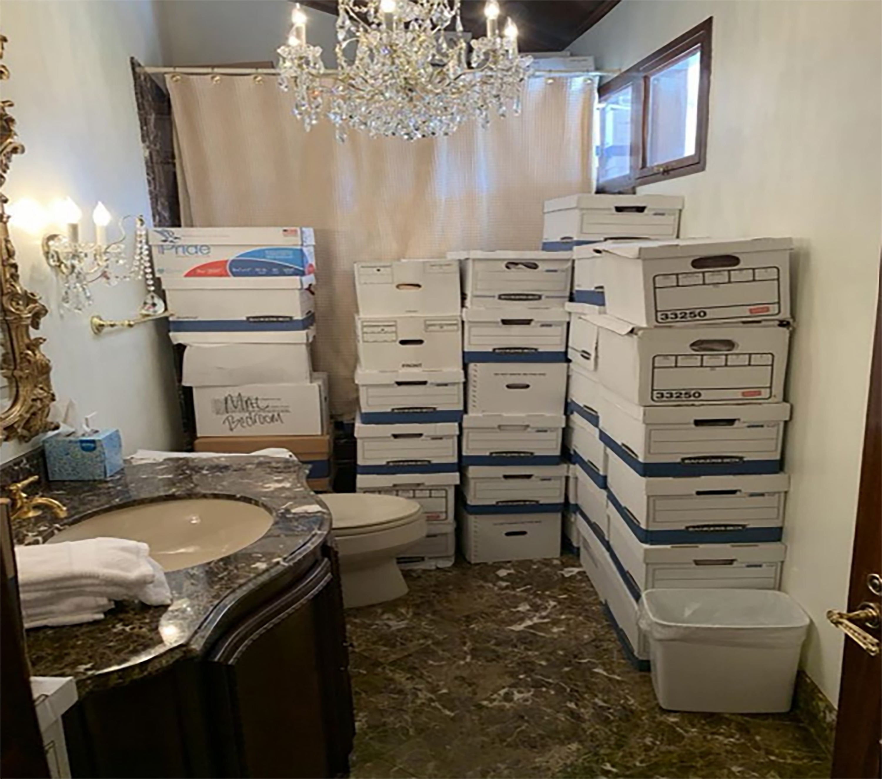 Kamar mandi dengan tumpukan kotak dokumen di samping toilet dan lampu kristal di atasnya