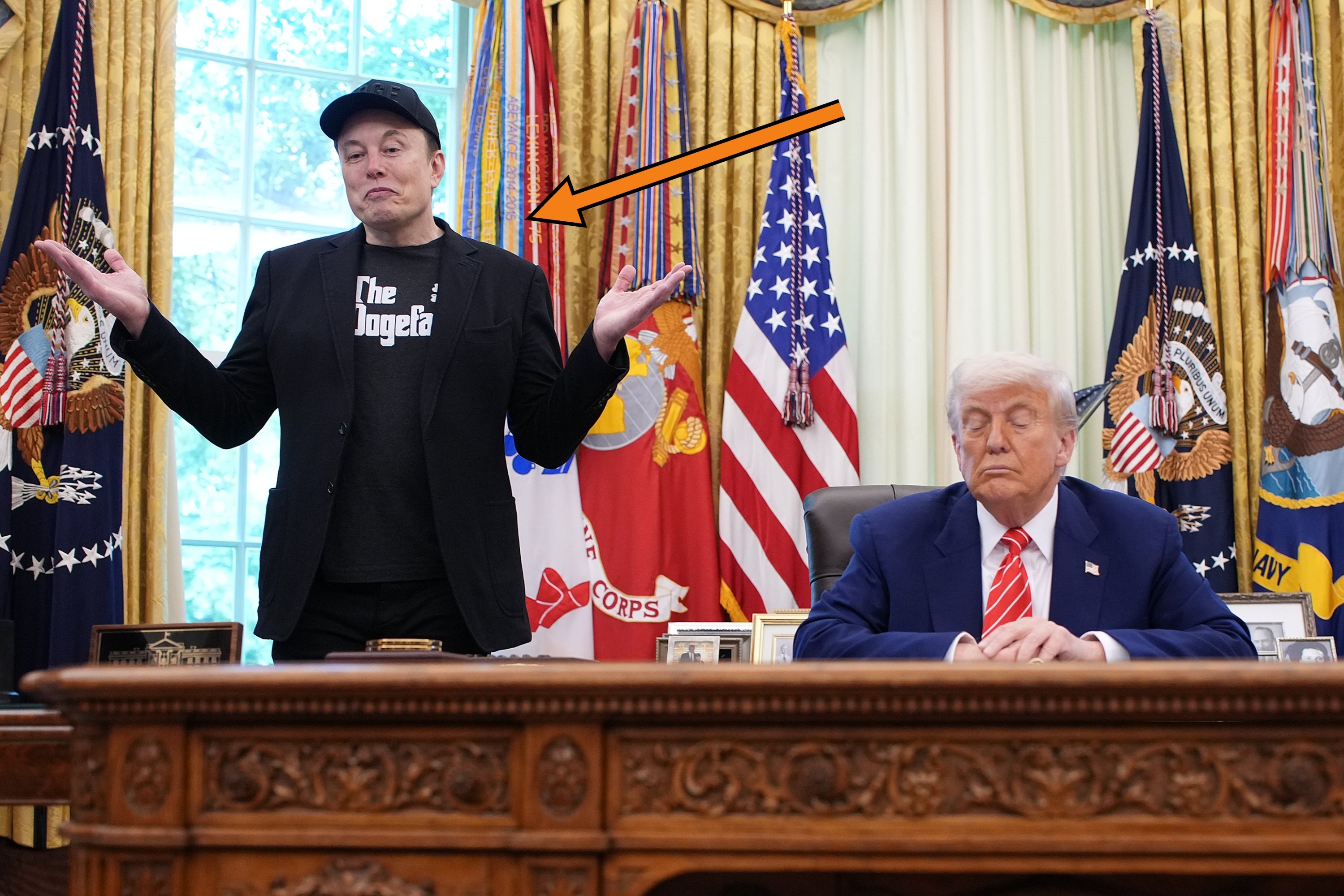 Elon Musk berdiri dengan tangan terbuka sambil mengangkat bahu di samping Donald Trump, duduk di belakang meja tegas di Ruang Oval