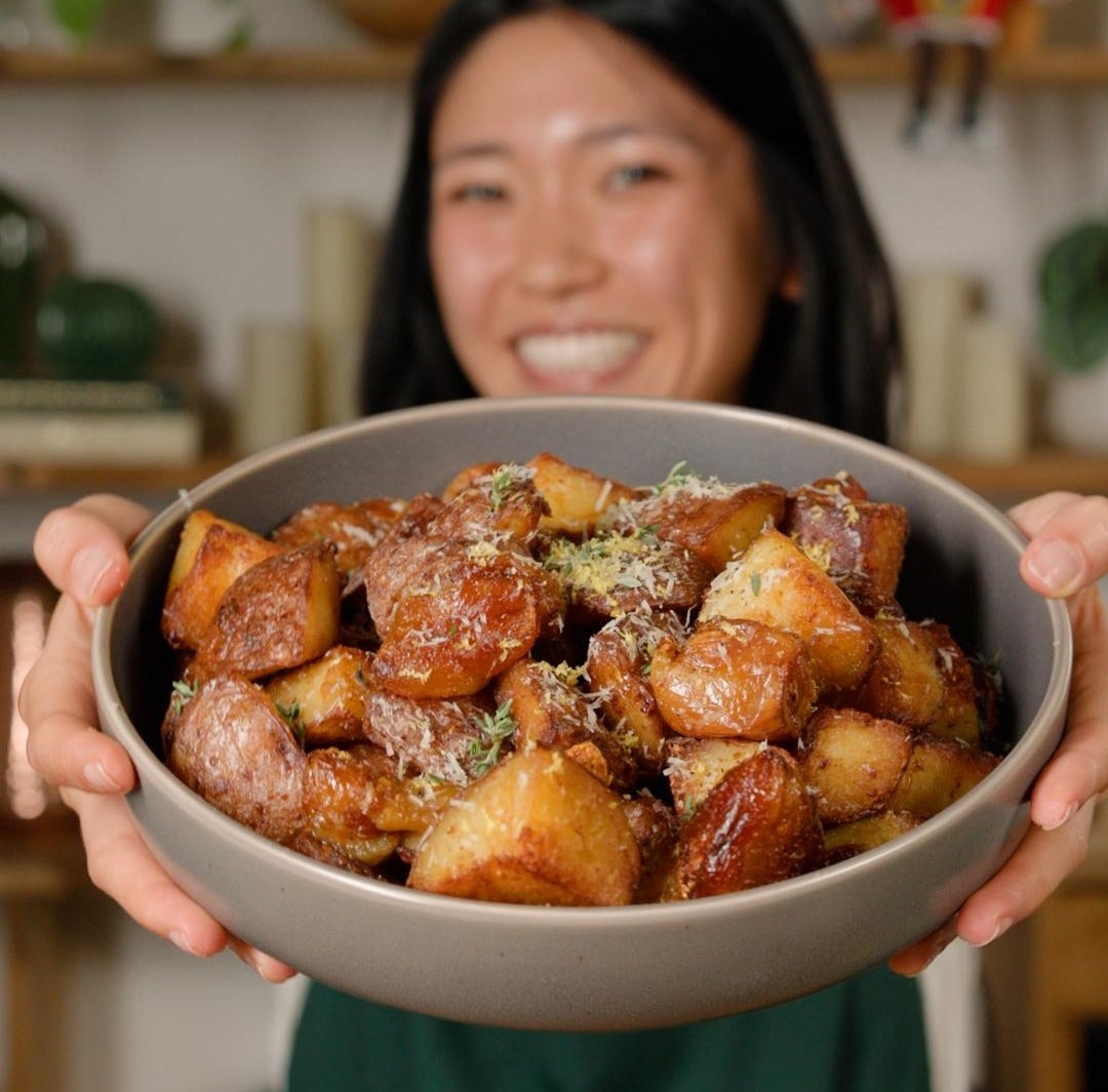 Person holding a vessel  of crispy roasted potatoes, smiling successful  a room  setting