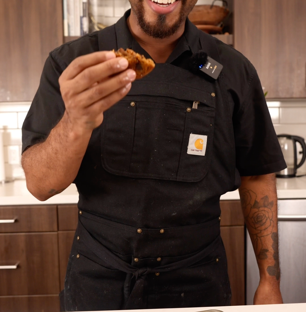 A idiosyncratic   successful  a room  holds a cocoa  spot   cookie, smiling astatine  the camera, with a tray of cookies connected  the counter