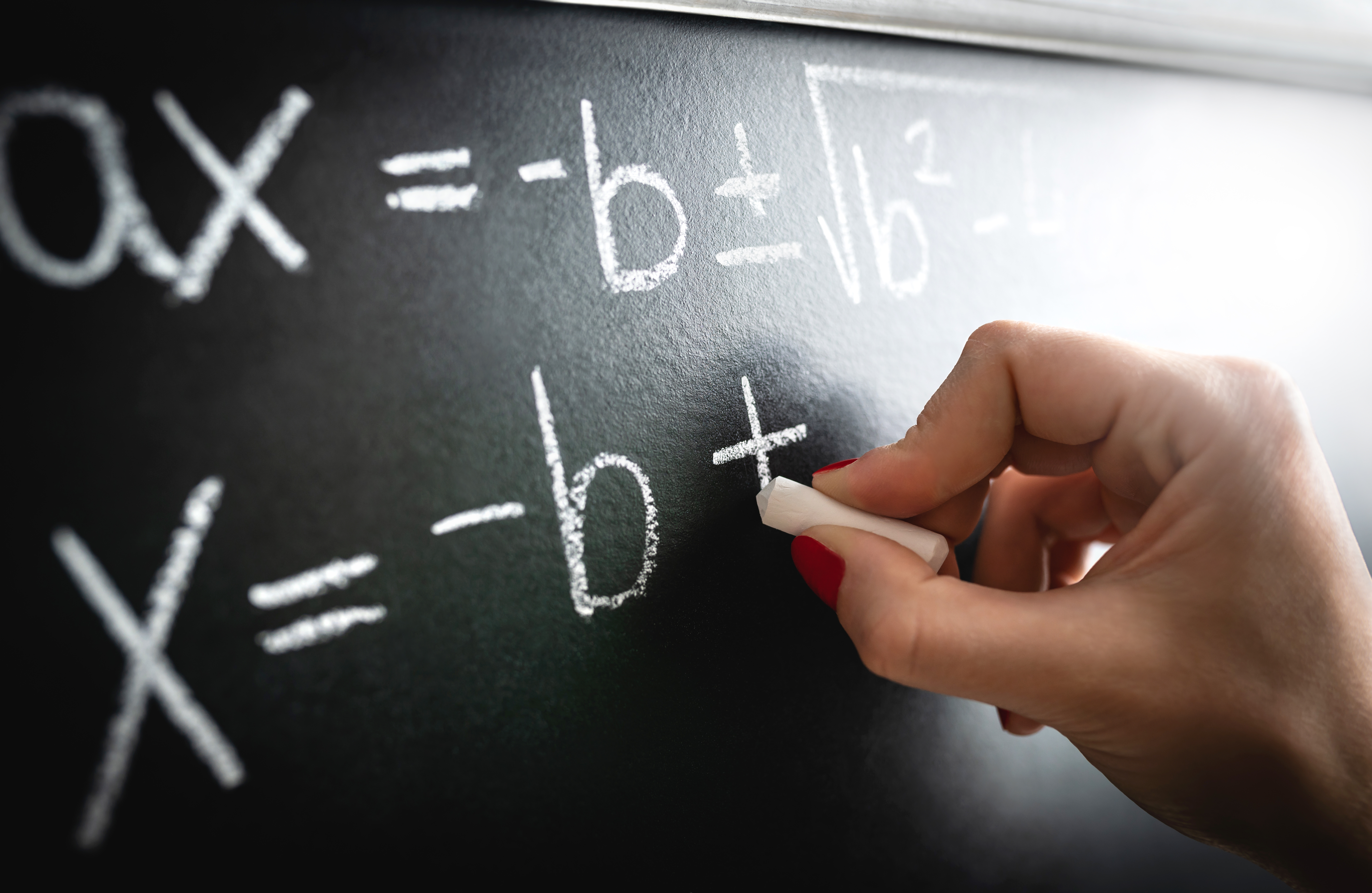 Hand penning a mathematical equation connected a chalkboard