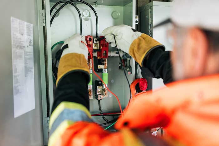 Electrician moving   connected  a circuit breaker panel, adjusting wires and components with protective gloves and gear