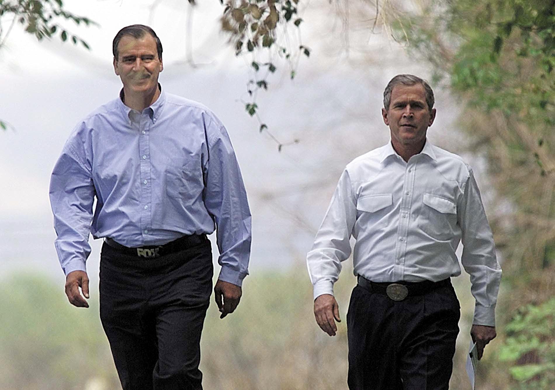 To menn går utendørs, iført langermede skjorter og bukser, i naturlige omgivelser med trær rundt seg