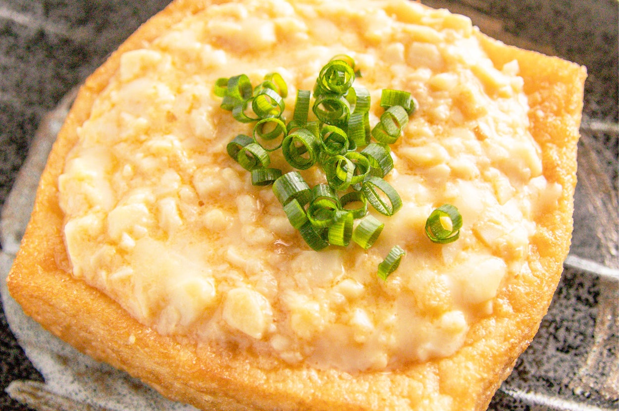 厚揚げの上に刻んだ青ネギが載せられている料理のクローズアップ。