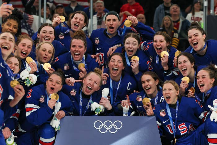US women's hockey celebrate with gold medals at the Olympics, smiling and posing for a group photo