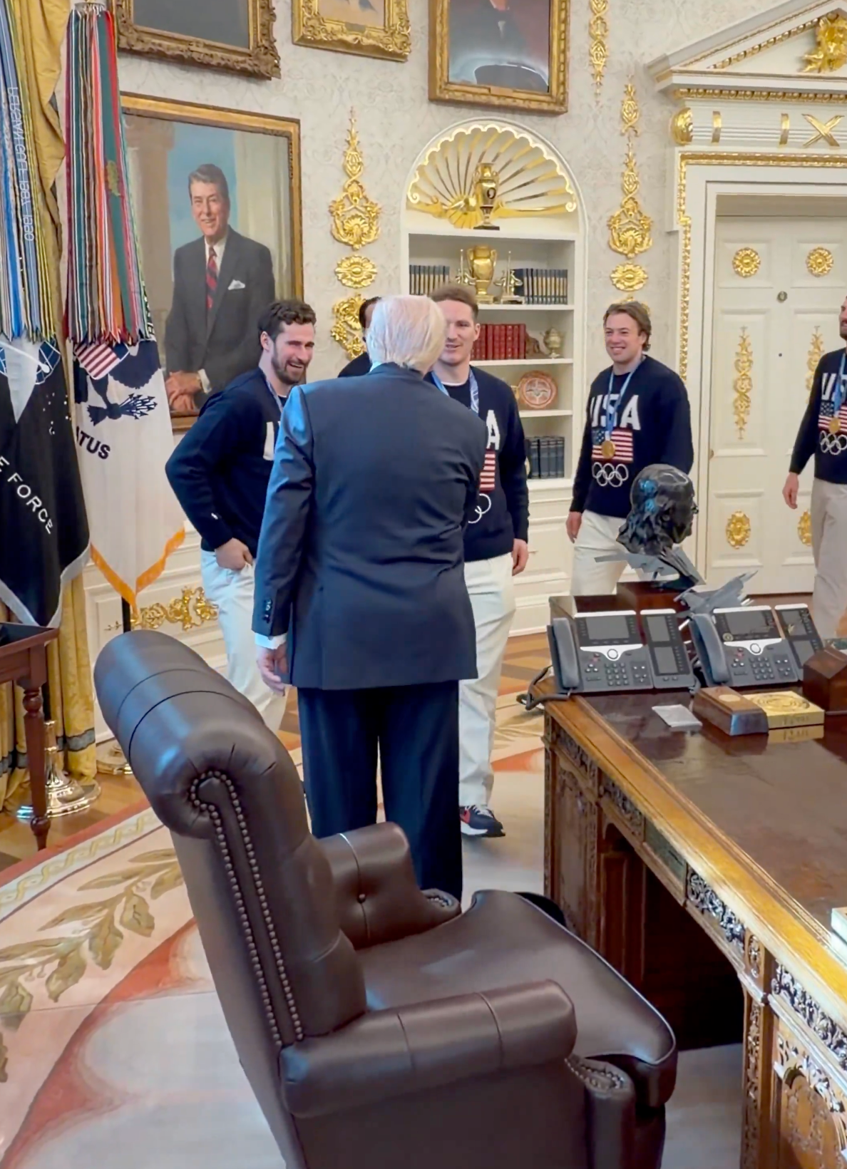 En gruppe mennesker i matchende USA-gensere møter en mann i dress på et utsmykket kontor