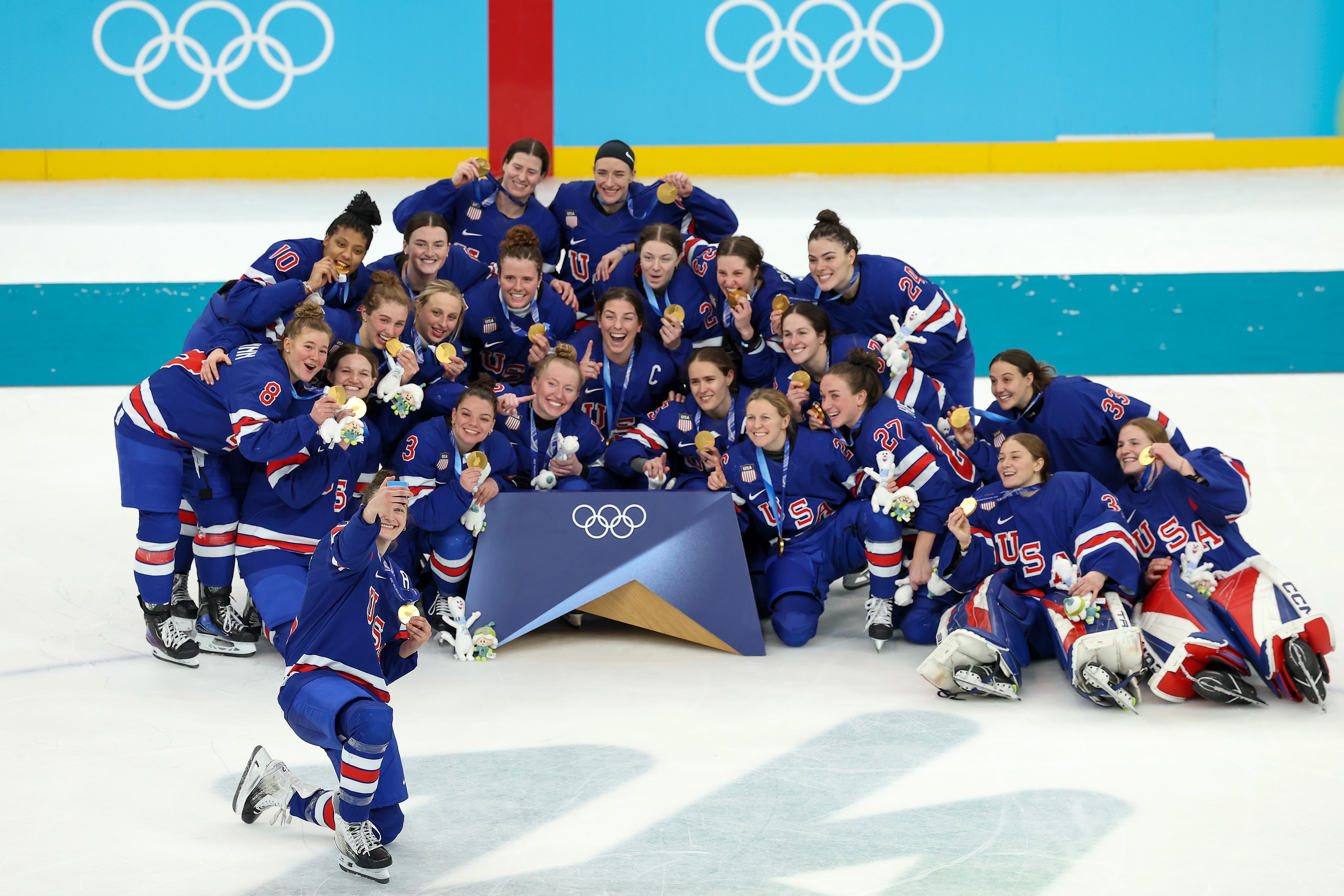 Et glad hockeylag poserer med gullmedaljene sine i OL, iført matchende uniformer og smilende til et gruppebilde på isen