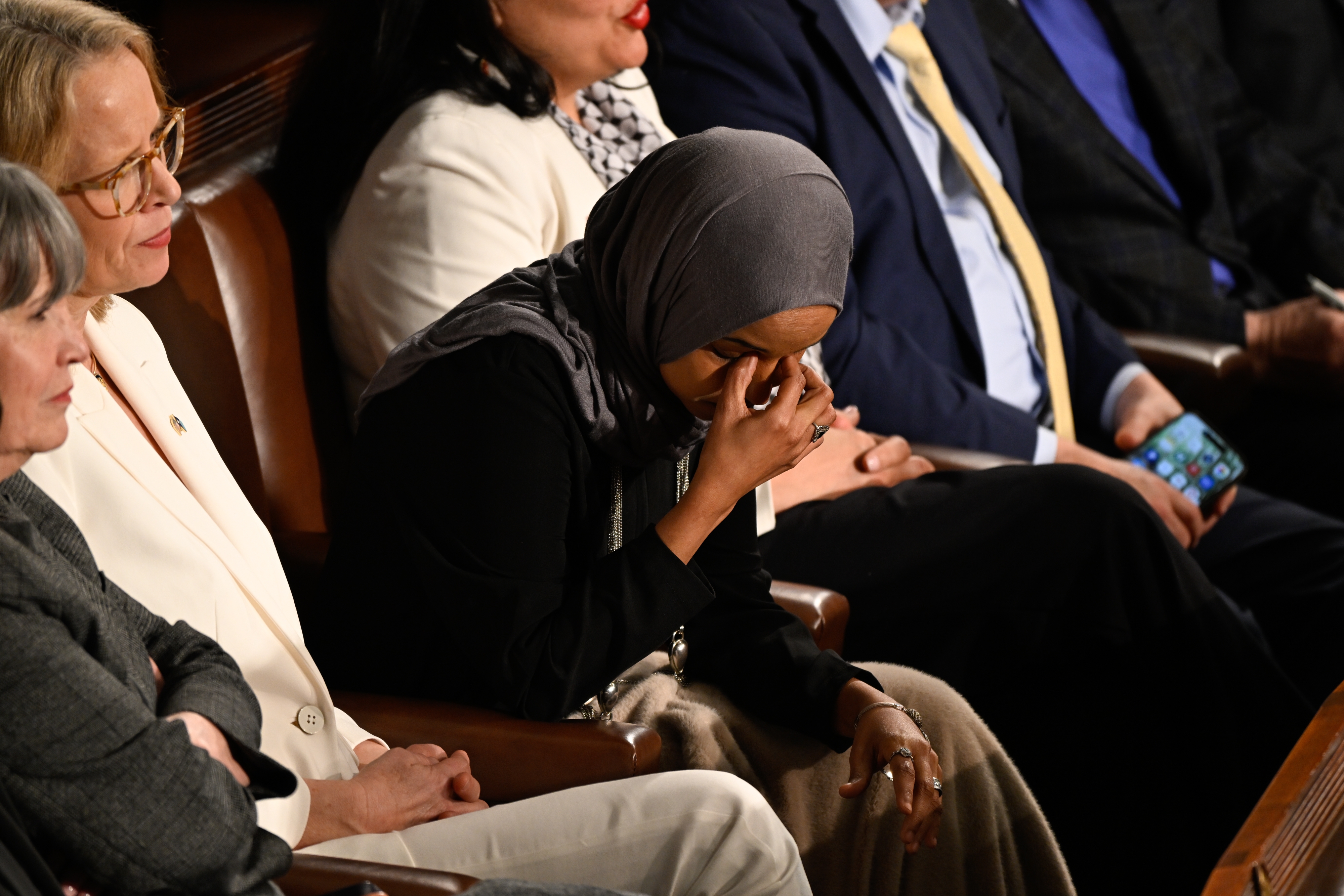 En person i et skjerf tørker øynene mens han sitter blant annet i formelle antrekk på et offentlig arrangement