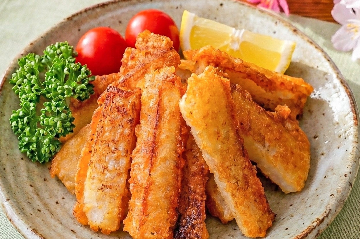 お皿に盛られた揚げた魚のフライ、プチトマト、パセリ、レモン添え。背景に桜の花飾り。