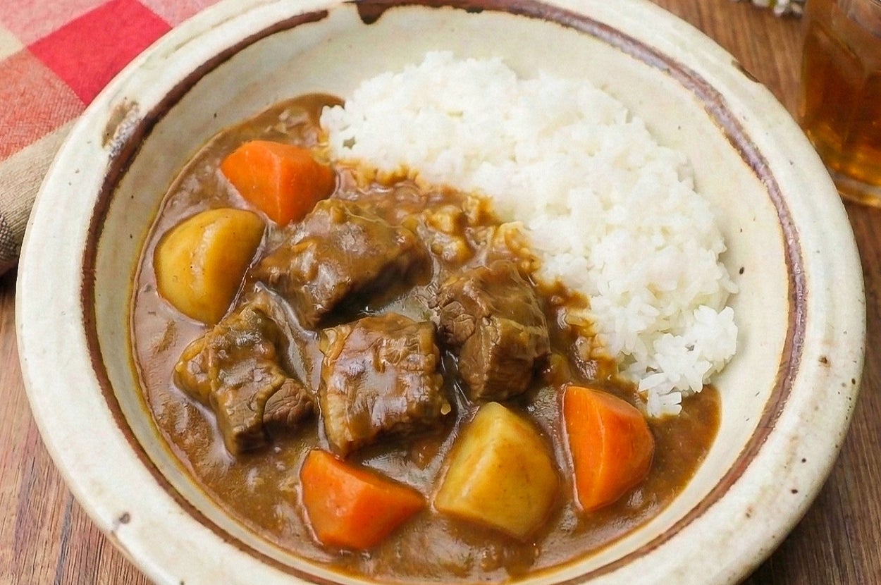 カレーライスの盛り付け。ごはんの横に牛肉、じゃがいも、にんじんのルーがかかっている。