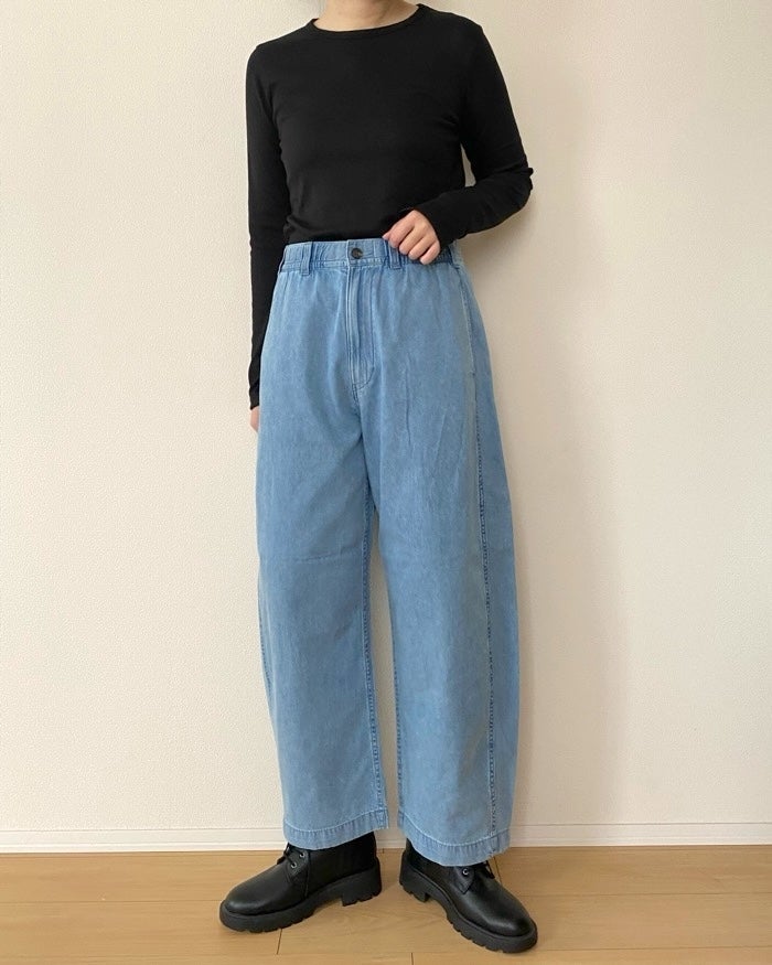 GUの「ライトデニムバレルレッグイージーパンツ（丈標準67.5～71.5cm）」黒い長袖トップスとゆったりしたデニムパンツを履いた人物が立っている。黒いブーツを履いている。