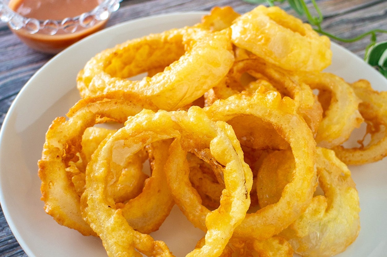 皿に盛られたカリッとしたオニオンリングと横にディップソース。背景は木製テーブル。