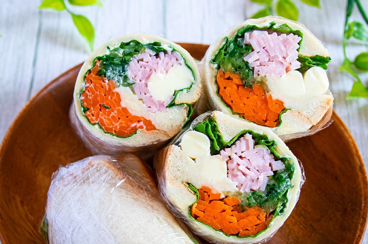 ラップサンドイッチが木製プレートに盛られている。中には野菜やハム。