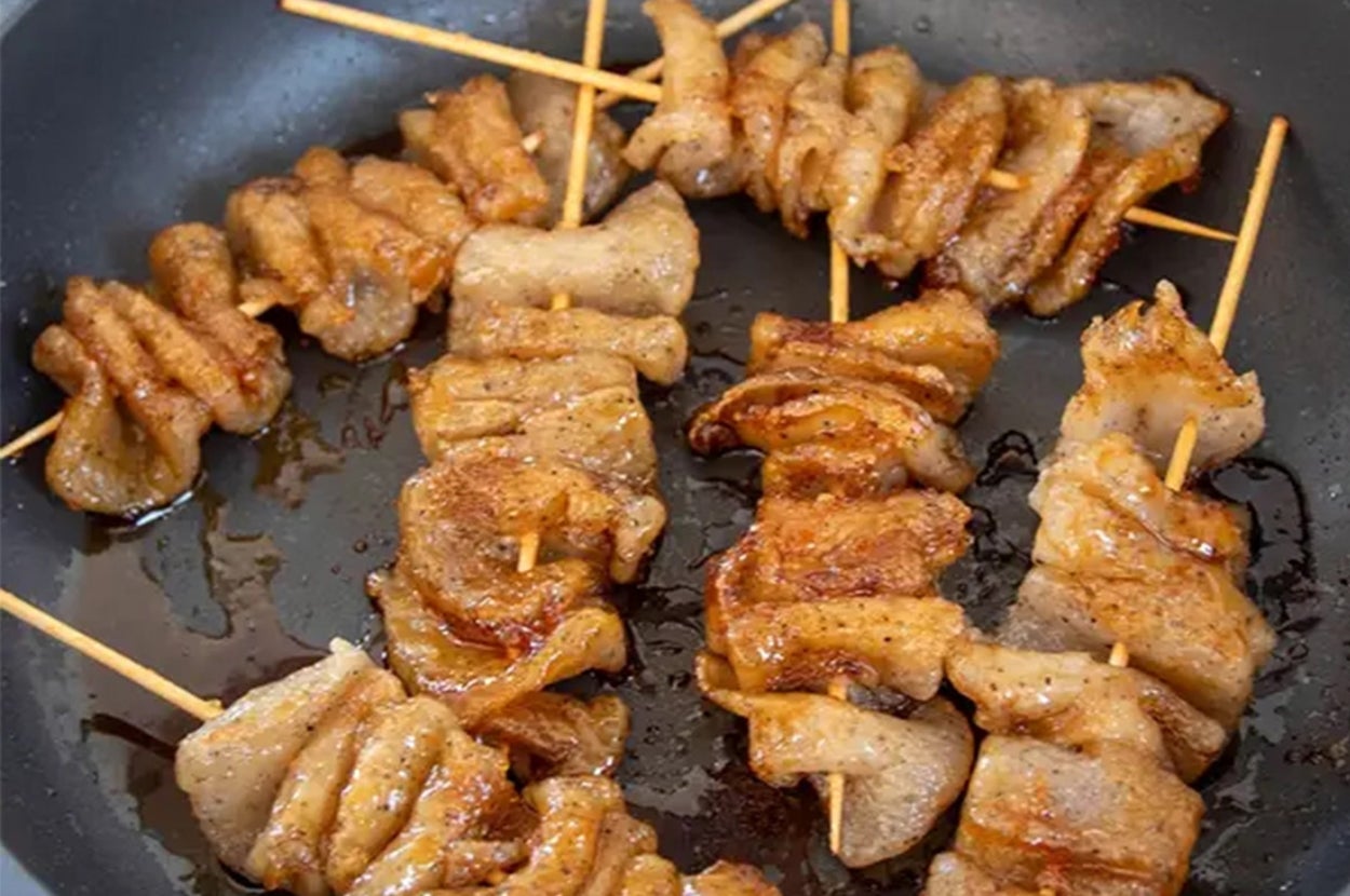 フライパンで焼かれている串に刺さったこんにゃく。調味料が絡まり、おいしそうな香ばしさを感じさせる。