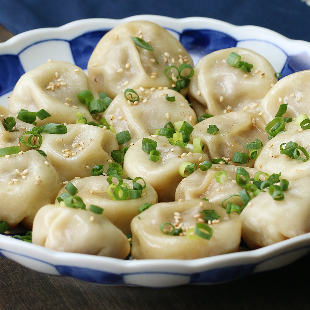 A bowl of steamed dumplings garnished with chopped green onions and sesame seeds on top