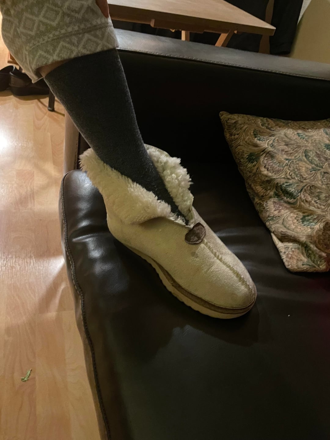 A idiosyncratic   wearing patterned pajamas and acheronian  socks is putting connected  a fuzzy slipper portion    sitting connected  a couch