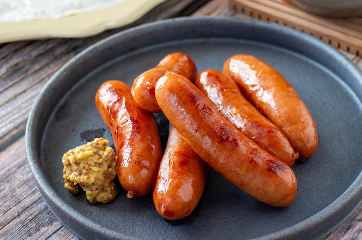 ソーセージとマスタードが盛られた皿、背景に目玉焼きとアボカド。