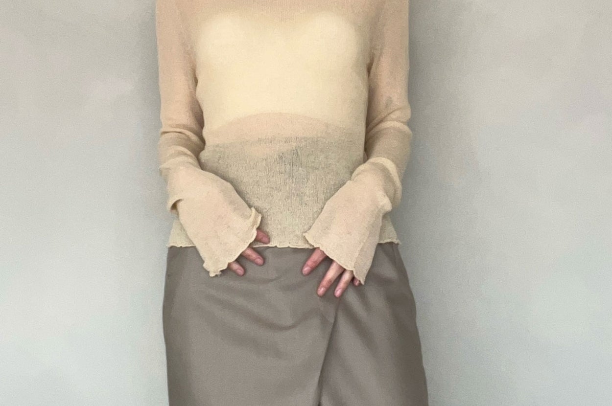 Person wearing a sheer turtleneck top with unique sleeve cuffs and a long, fitted skirt standing against a plain backdrop