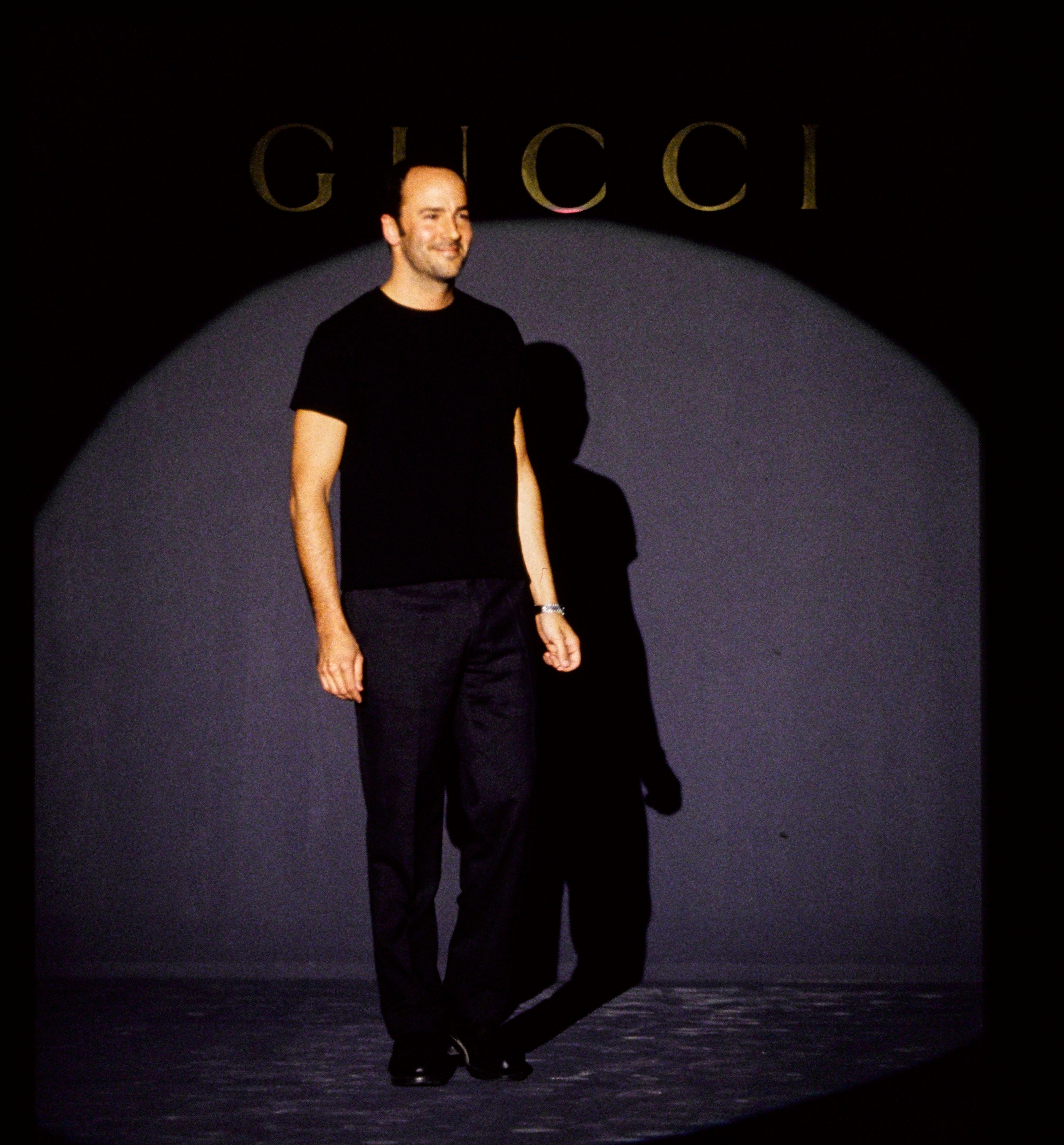 A idiosyncratic stands connected a signifier successful simple, stylish attire with a achromatic garment and pants, nether a spotlight, successful beforehand of a Gucci backdrop