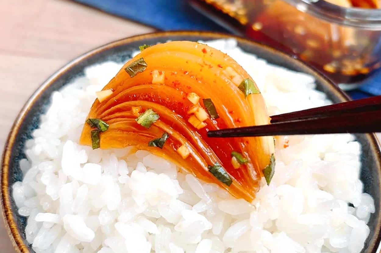 ライスボウルの上にキムチが盛られ、箸で持ち上げられている場面。背景にガラス容器が見える。