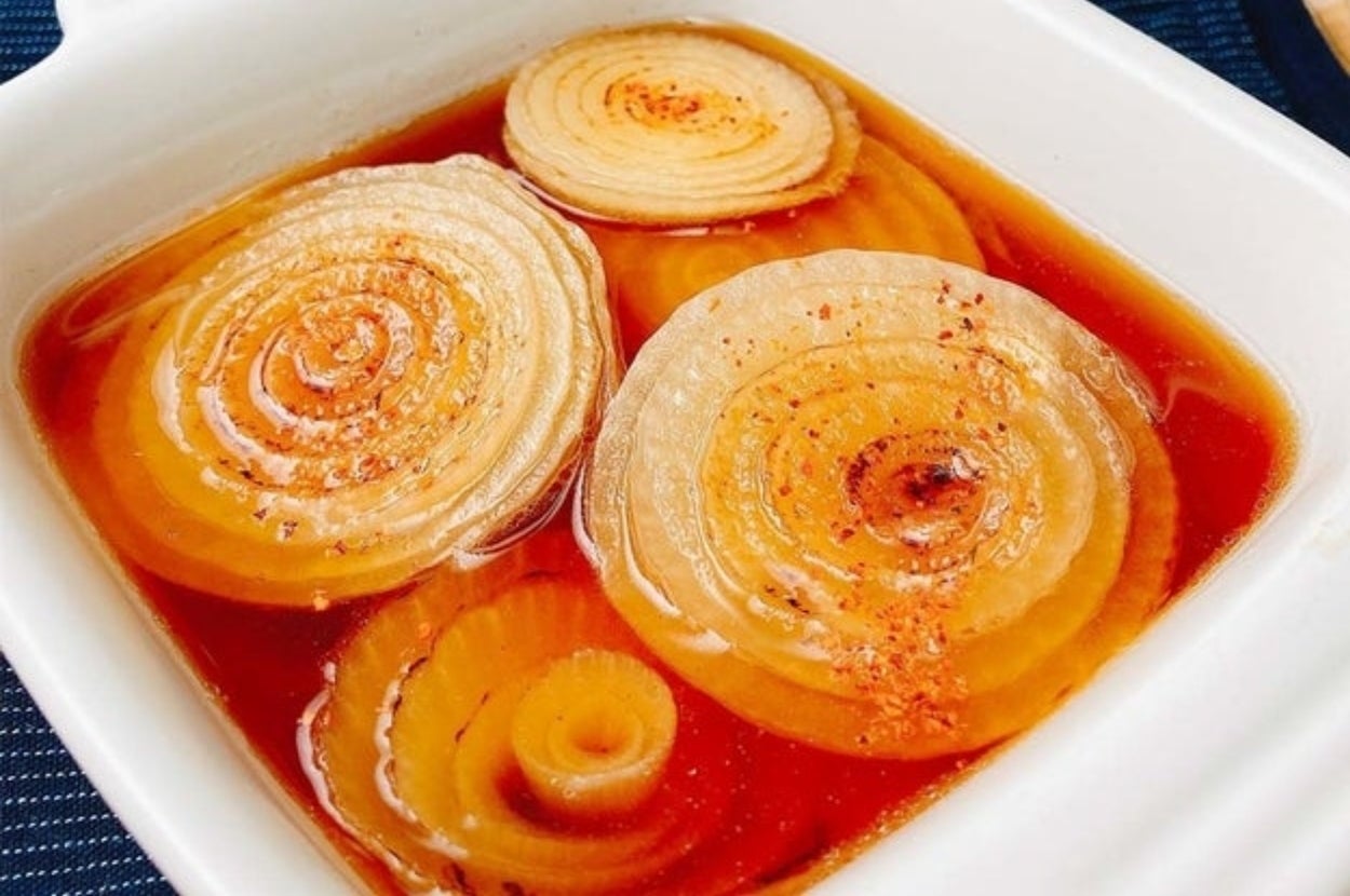 タマネギがスープに浸っている料理。背景に数個の丸ごとのタマネギが見える。