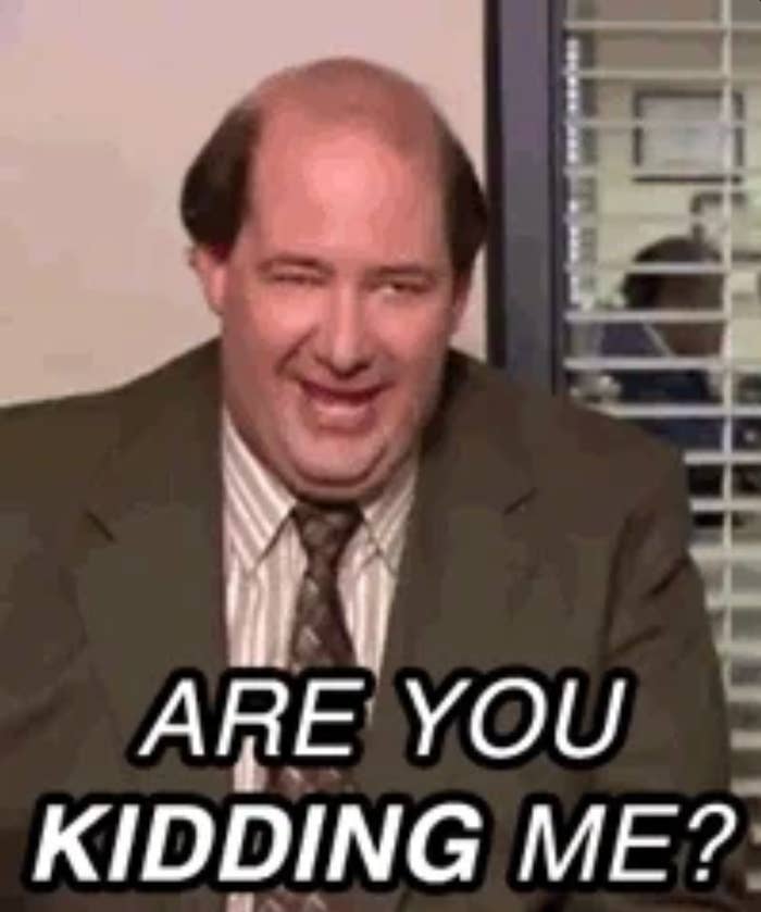 A antheral   sitting successful  an bureau   setting, smiling and laughing with substance   connected  the representation  reading, "ARE YOU KIDDING ME?"