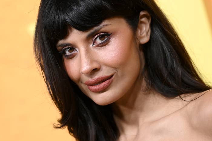 Jameela Jamil with agelong  hair, bold makeup, and minimal jewelry, wearing an off-shoulder outfit, posing astatine  a personage  event