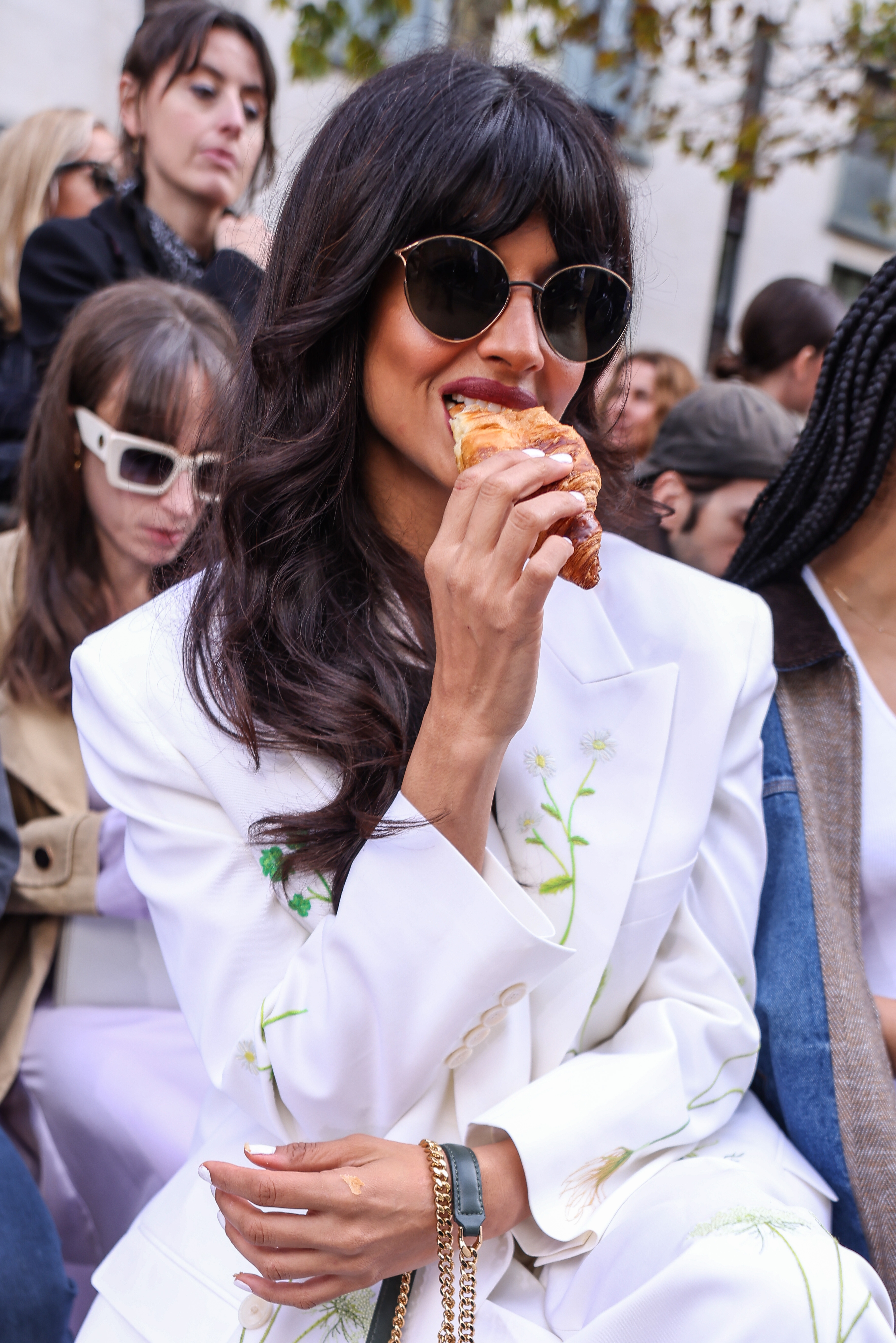 Jameela Jamil successful  an embroidered suit   and sunglasses, sitting among others, eating a pastry