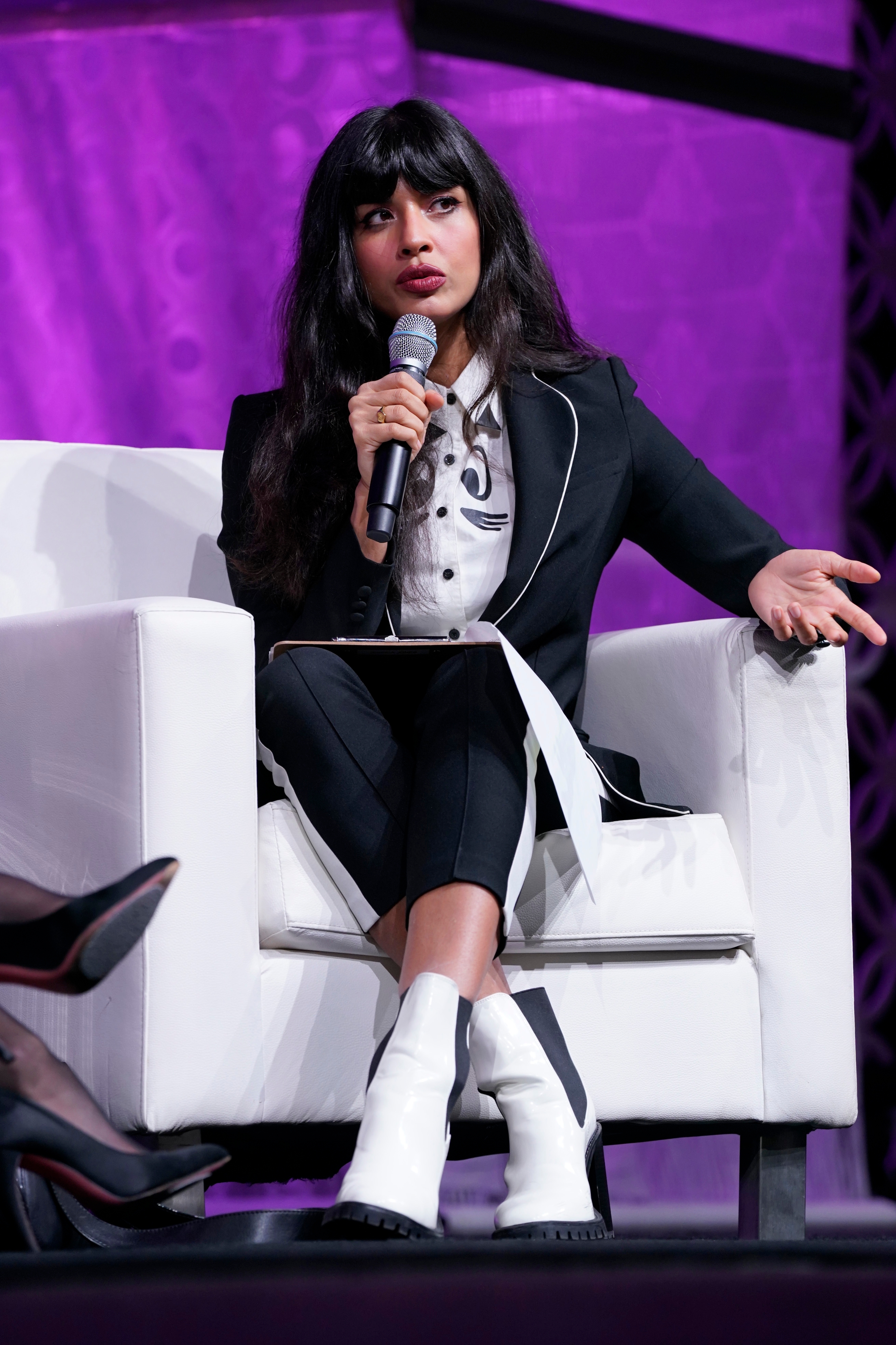 Jameela Jamil sits connected  a signifier    successful  a suit   with ankle boots, holding a microphone and gesturing portion    speaking