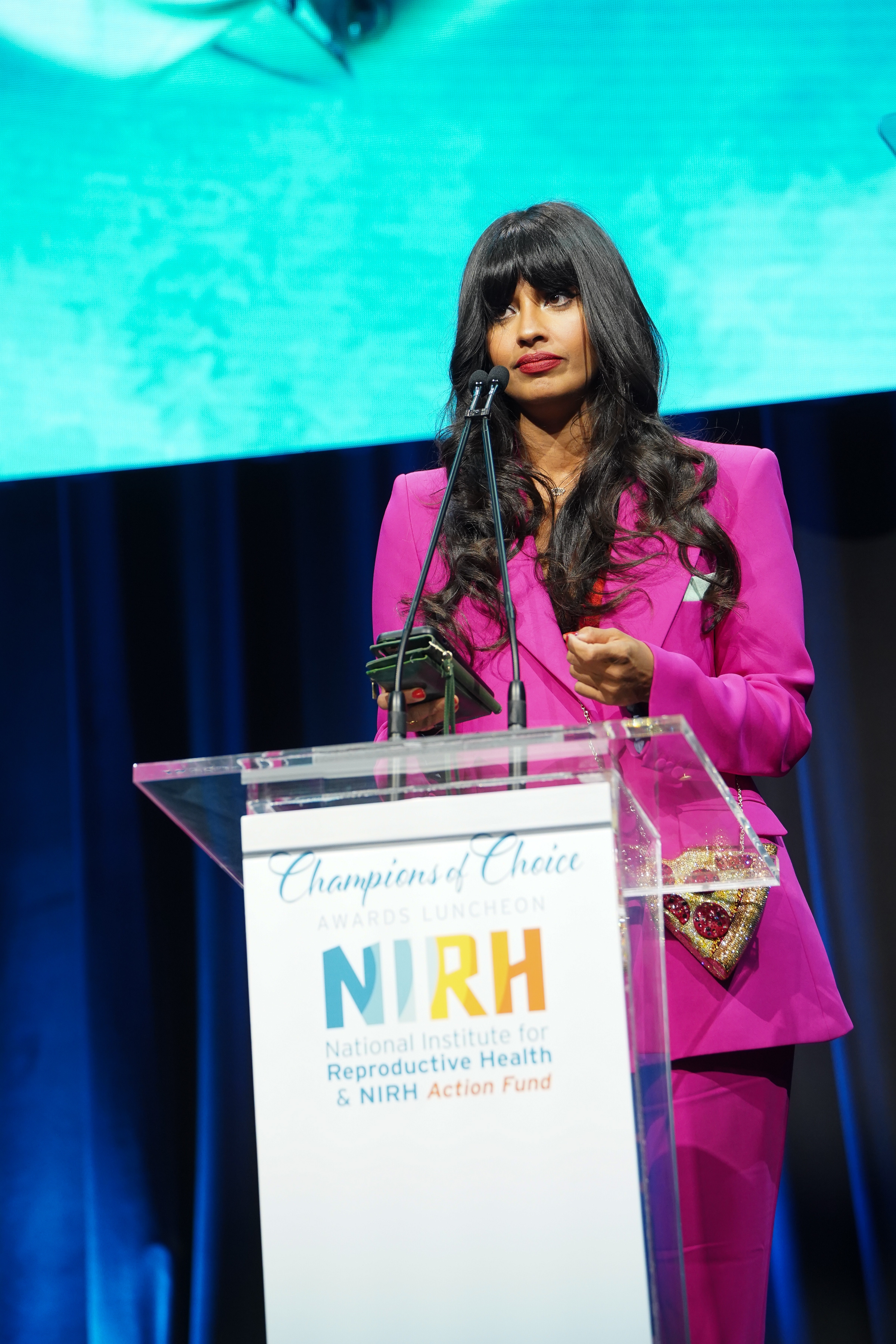Jameela Jamil successful  a stylish suit   speaks astatine  a podium during an grant  event