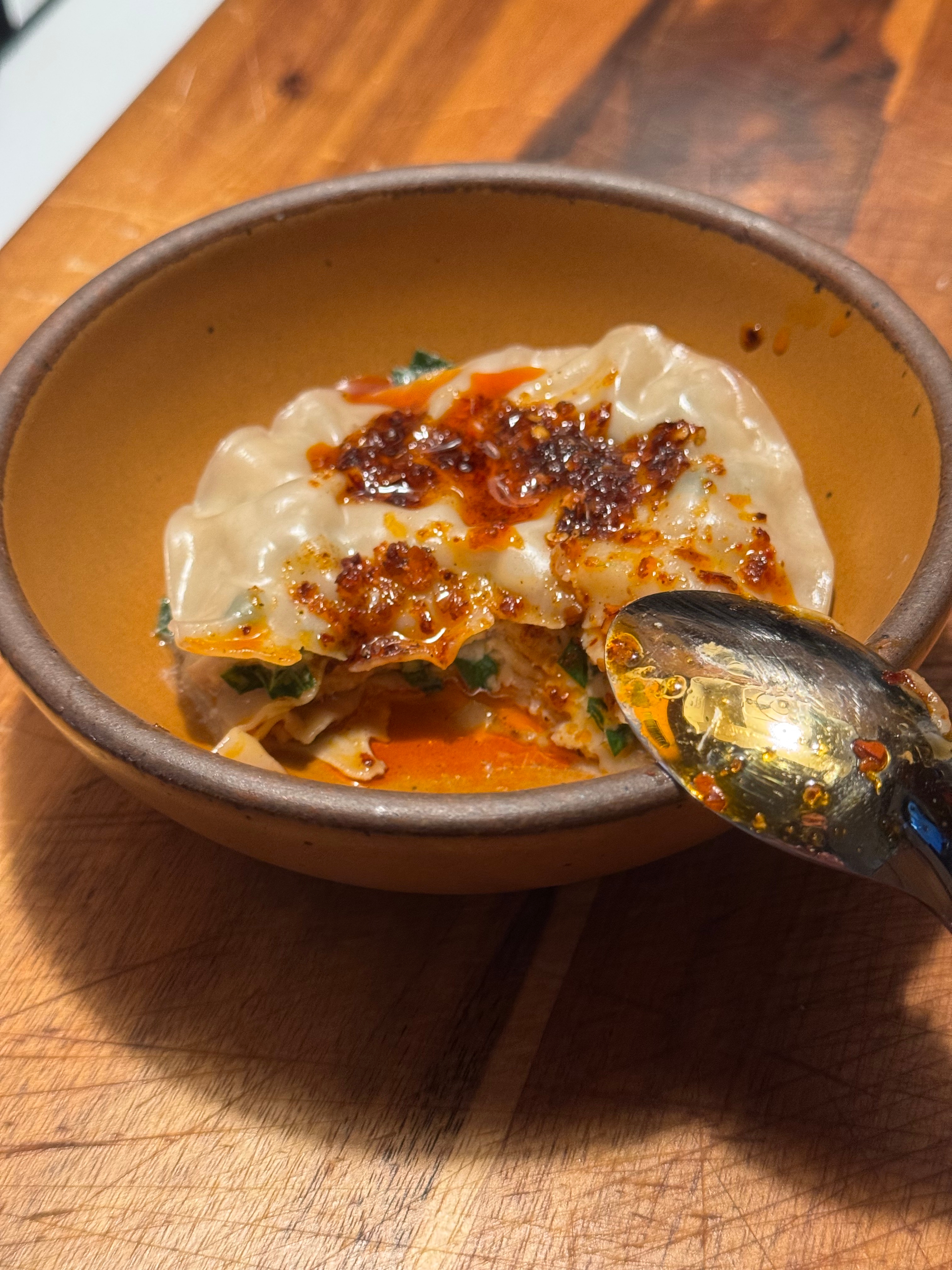 A bowl of dumplings topped with spicy chili oil, garnished with herbs, and a spoon resting on the side