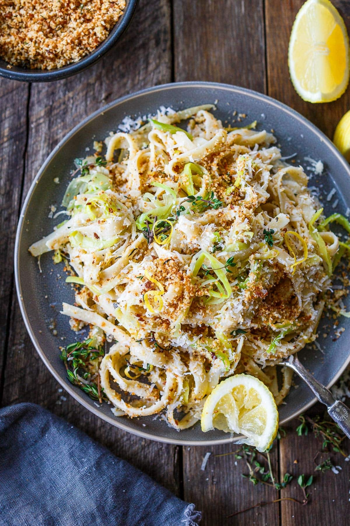 Plate of fettuccine pasta topped with grated cheese, crispy breadcrumbs, citrus slices, and caller herbs