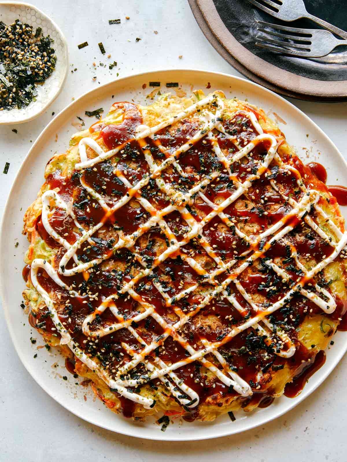 Plated okonomiyaki topped with zigzagged mayonnaise, sauce, and sprinkled with sesame seeds and nori