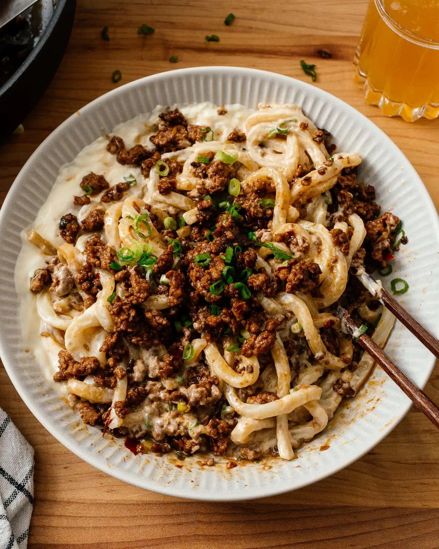 A sheet of creamy noodles topped with spicy minced meat, garnished with chopped scallions. A solid of portion sits nearby