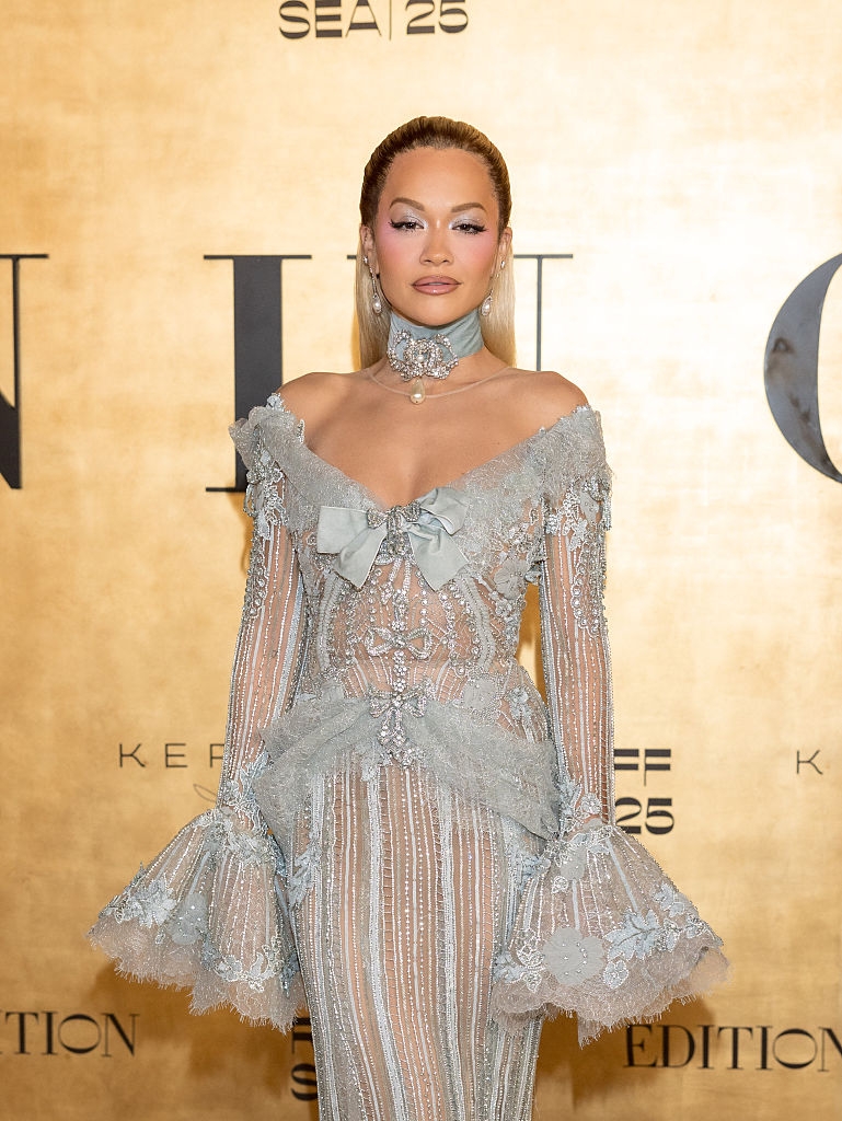 Celebrity successful an intricate, lace gown with off-shoulder plan and flared sleeves, posing connected a reddish carpet astatine a media lawsuit backdrop