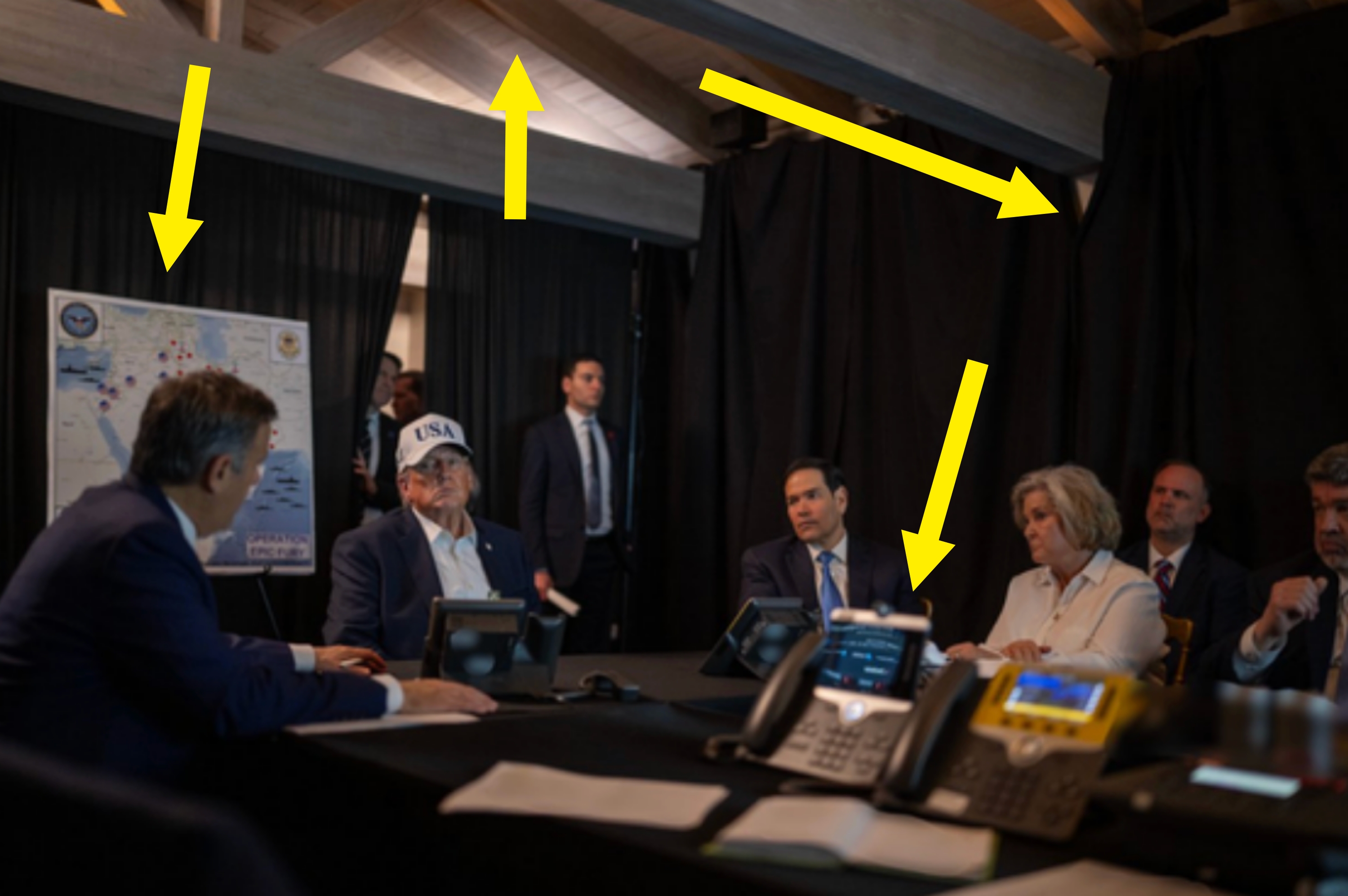 People successful a gathering room, immoderate successful suits and 1 wearing a cap, astir a league array with phones and seated attendees successful discussion