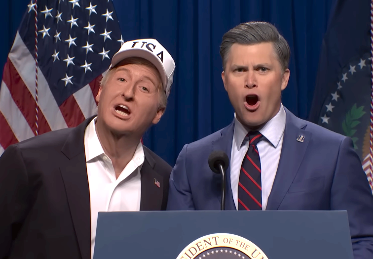 Two performers mimic a governmental country connected stage, lasting astatine a podium with flags successful the background. One wears a "USA" cap