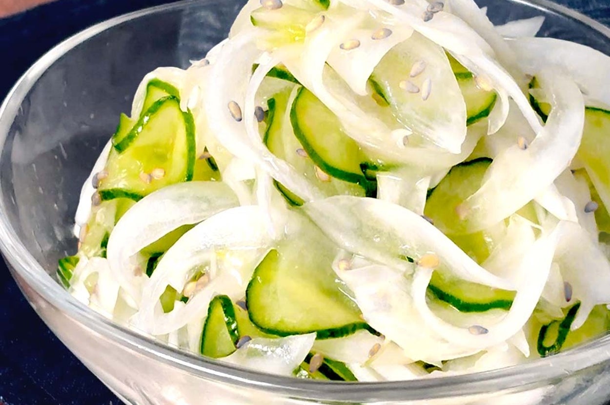 薄切りの玉ねぎときゅうりのサラダがガラスのボウルに盛られている。白ごまがトッピング。